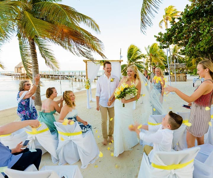 A newlywed couple walks down a beach aisle as guests celebrate with flower petals.