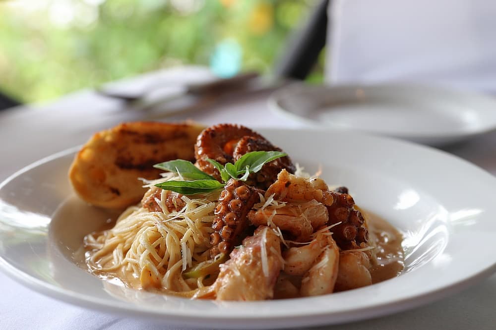 A plate of seafood pasta with octopus, shrimp, and fresh herbs, accompanied by toasted bread.