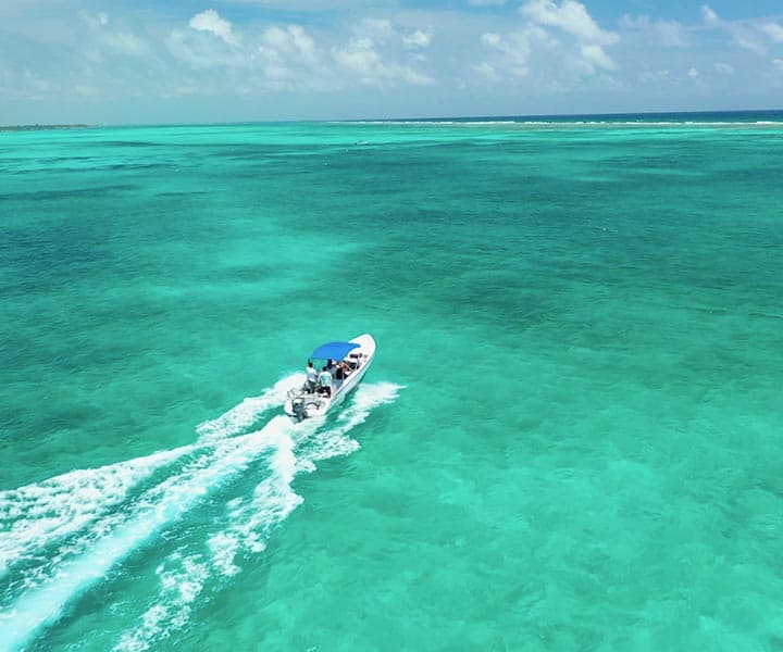 A boat glides over clear turquoise waters under a bright blue sky.