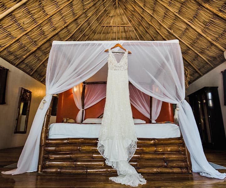 A wedding dress hangs gracefully above a bed in a rustic, elegantly decorated room.