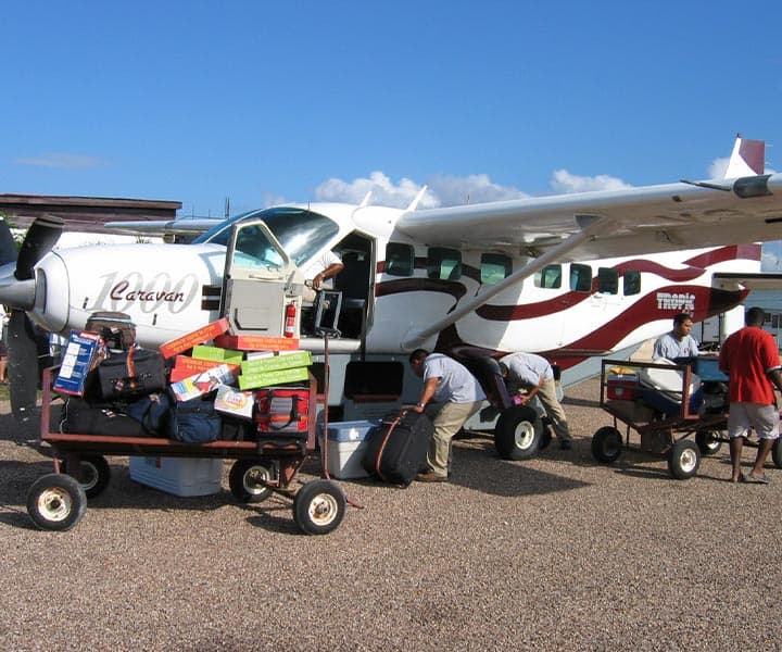 Ground crew loading luggage onto a small airplane beside a clear blue sky.