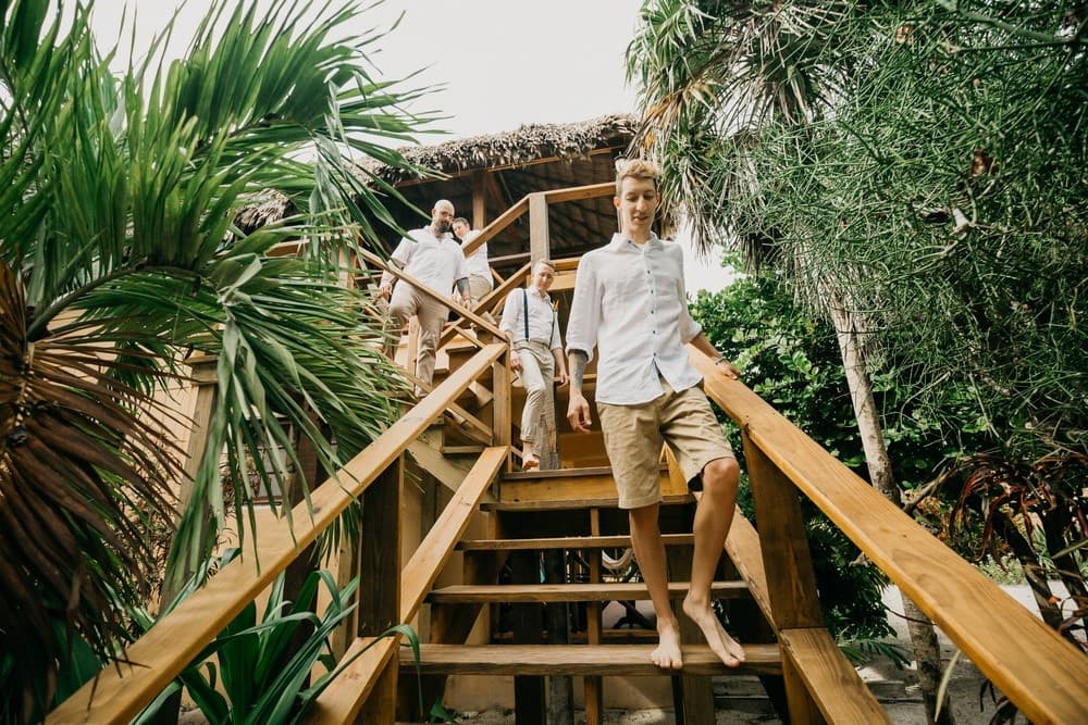 A group of three people, casually dressed, descends wooden stairs surrounded by tropical plants.