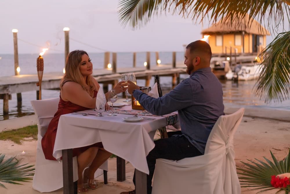 A couple toasts with drinks at a romantic beachfront dinner.