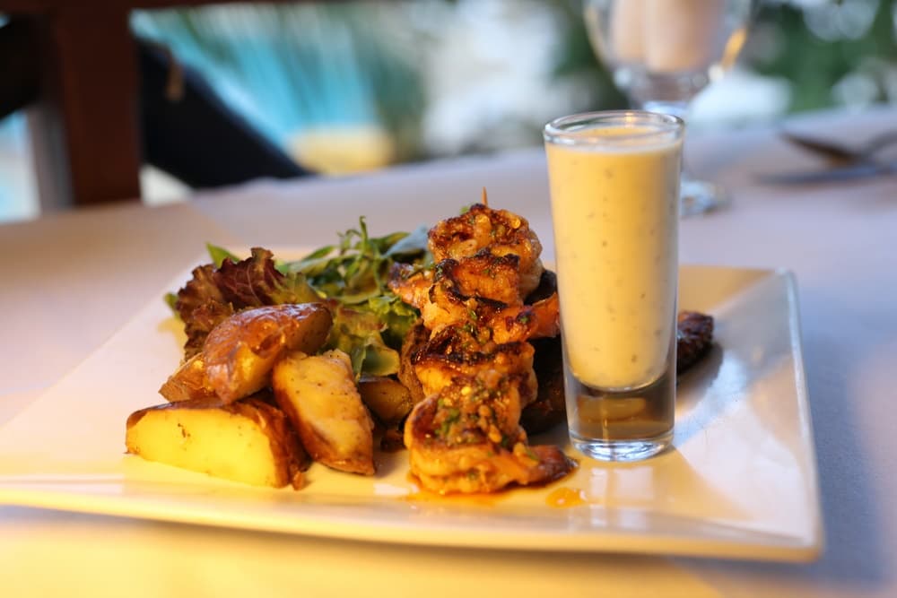 A plate of grilled shrimp with seasoned potatoes and a small glass of dipping sauce.