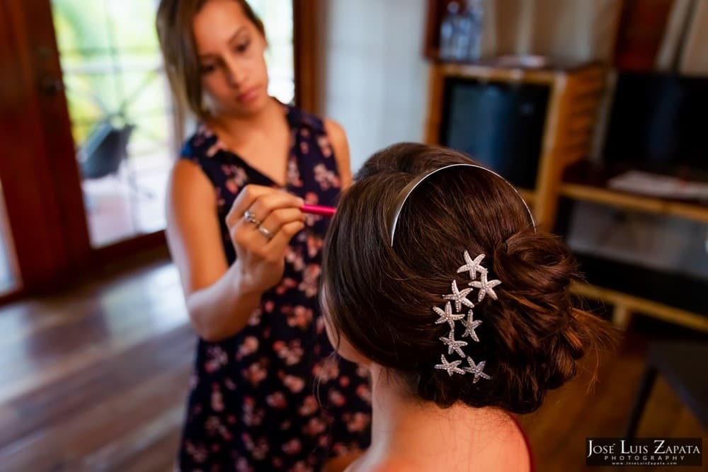 A stylist applies makeup to a woman with a stylish updo adorned with starfish hair accessories.
