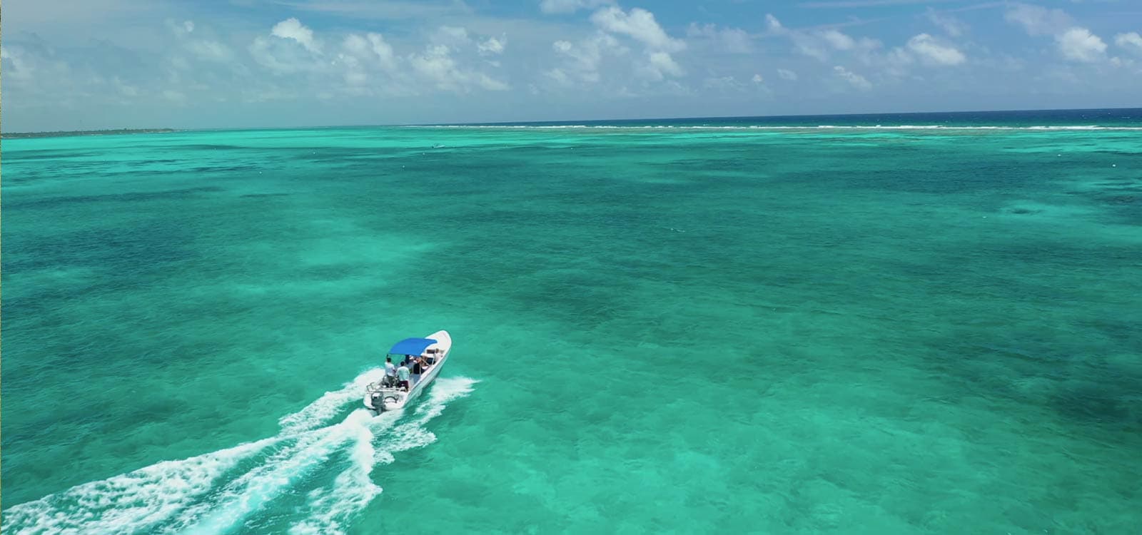 A small boat with a blue canopy speeds across clear, turquoise ocean waters under a blue sky, evoking a sense of adventure and freedom.