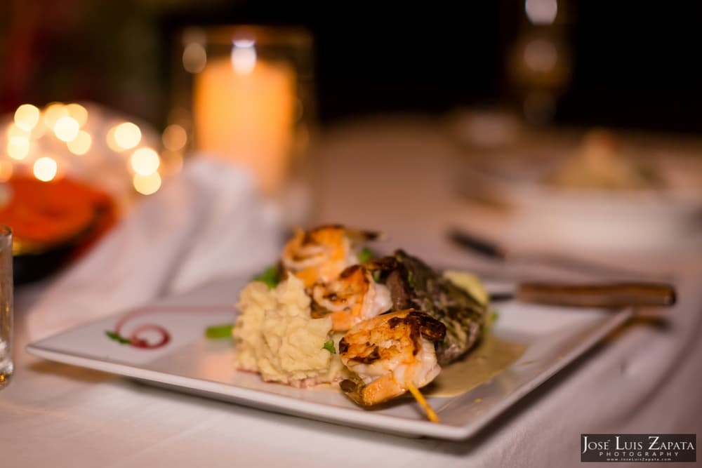 A gourmet plate with shrimp skewers served over creamy mashed potatoes, set in a dimly lit dining atmosphere.