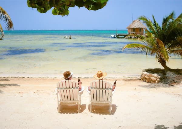 Two people in beach chairs enjoy drinks by the shore on a sunny day.
