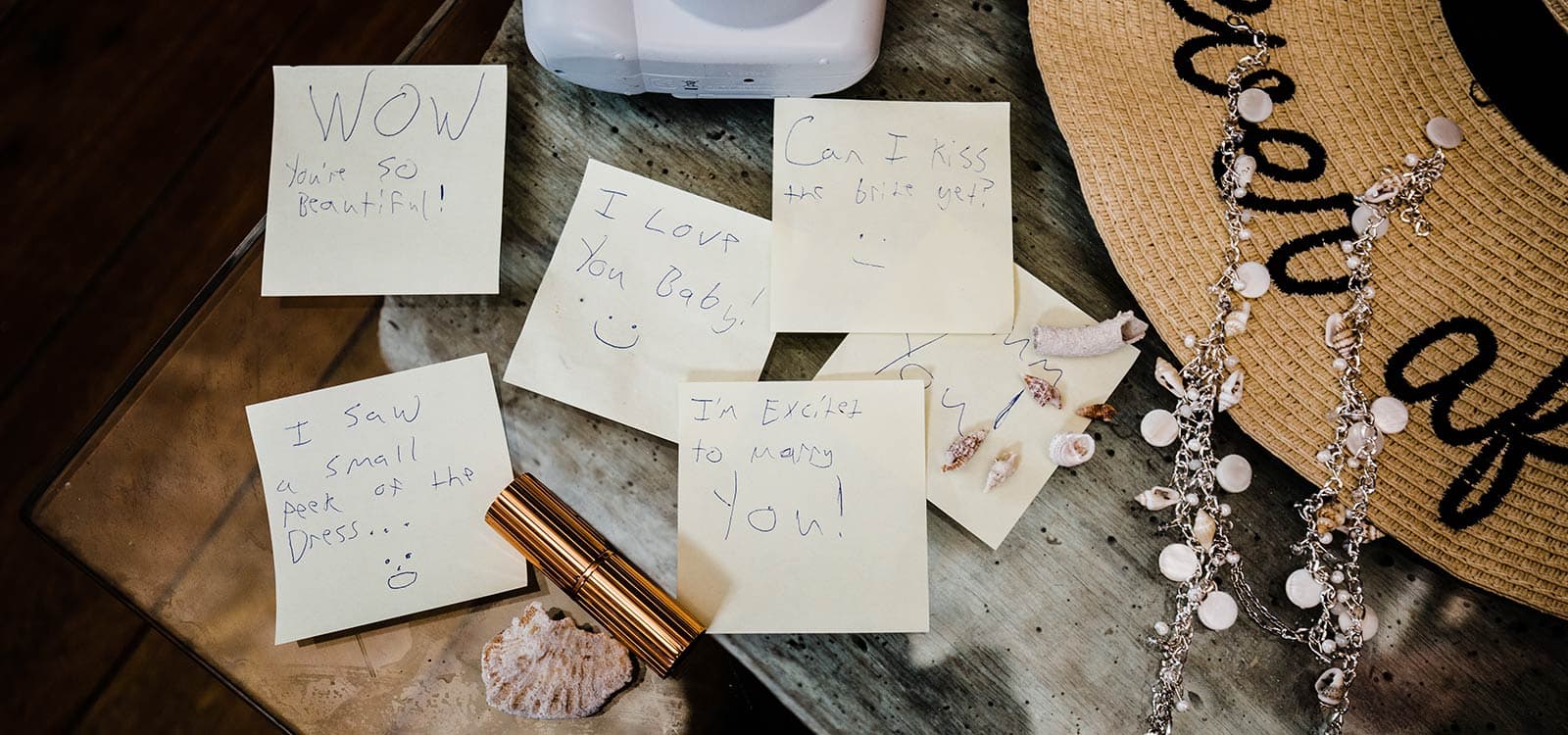 Sticky notes with loving messages like "You're so beautiful!" and "I love you, Baby!" are scattered on a table with seashells, a hat, and jewelry, conveying romance and excitement.