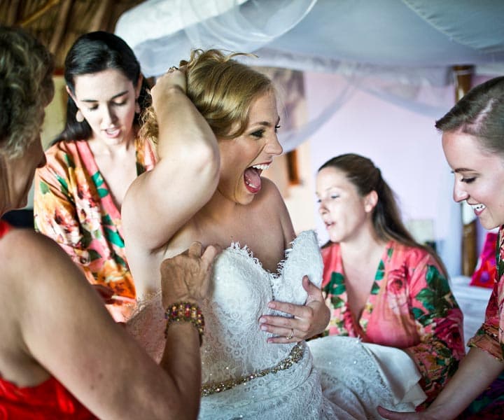 A bride excitedly laughs while getting dressed with the help of her friends.