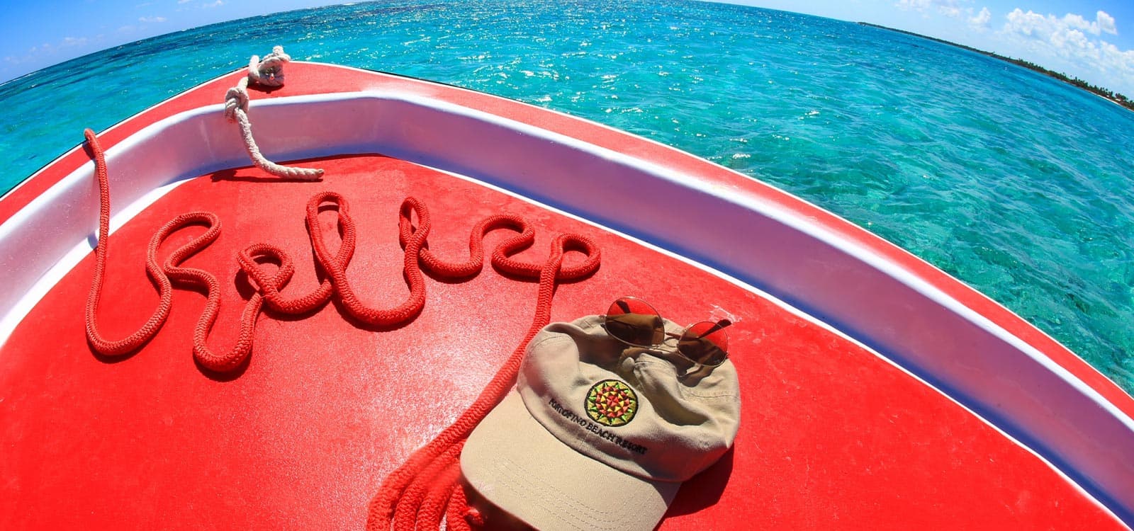 A red boat deck with "hello" spelled in rope, a beige hat, and a clear aqua sea in the background under a sunny blue sky, conveying relaxation.