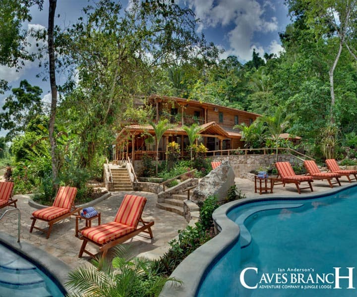 A tropical lodge with a pool surrounded by lounge chairs and lush greenery.