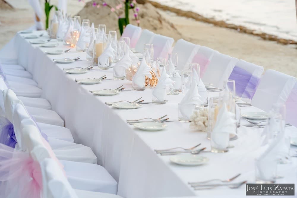 An elegantly set outdoor dining table by the beach with white tablecloths and decorative napkins.