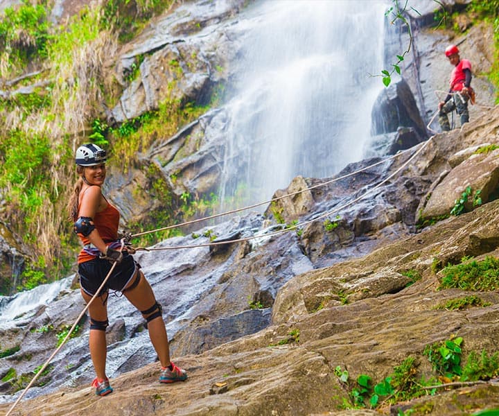 A climber prepares to rappel down a rocky waterfall with another climber in the background.