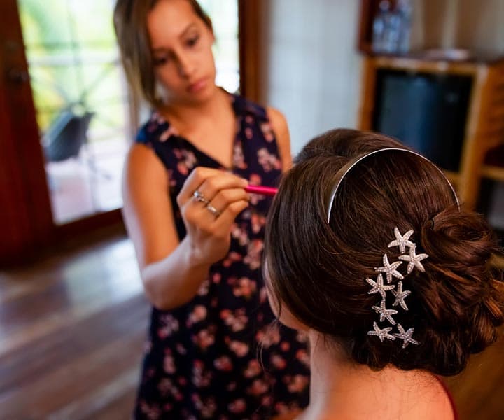 A stylist applies makeup to a bride with a starfish hair accessory.