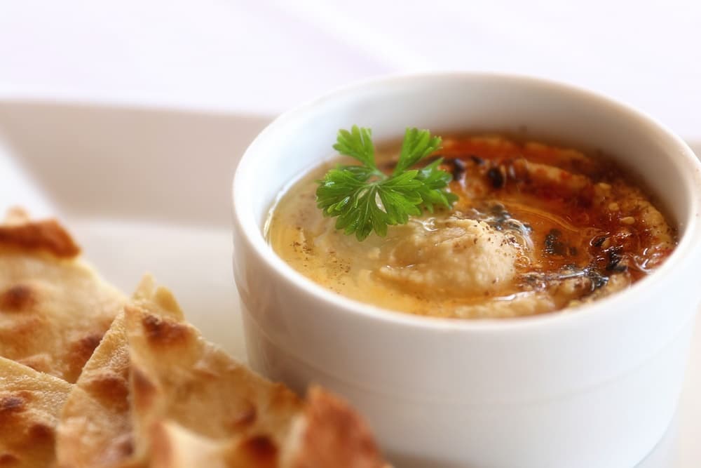 A bowl of hummus garnished with a sprig of parsley, accompanied by crispy flatbread.