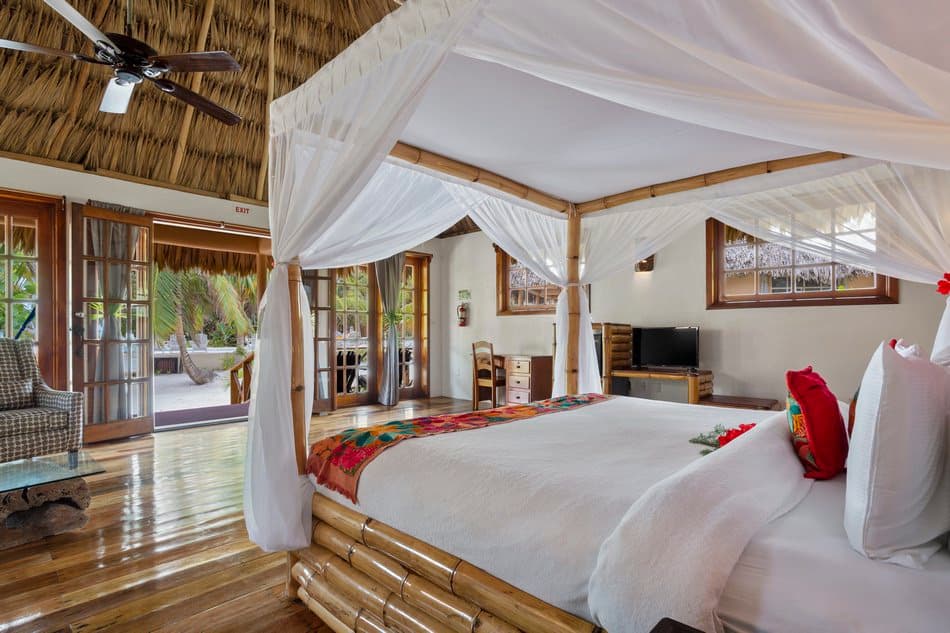 A beautifully decorated bedroom with a four-poster bed, wooden furniture, and large windows opening to a lush outdoor view.