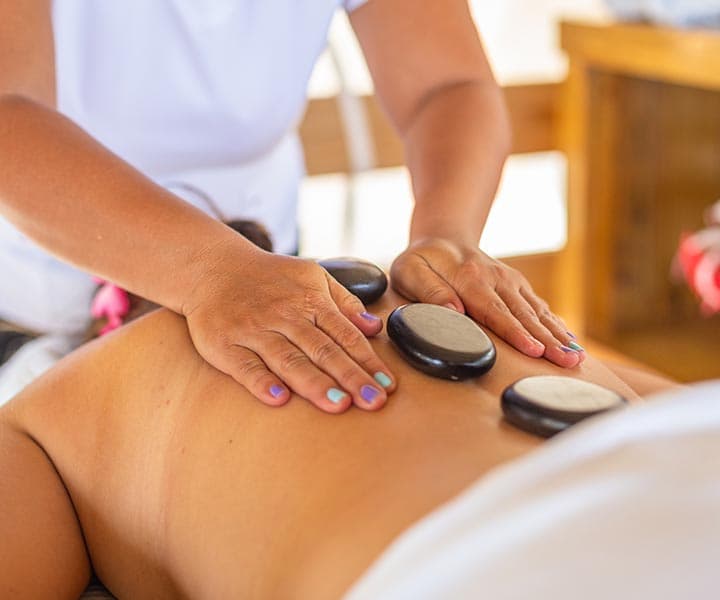 A massage therapist applies heated stones on a client's back during a treatment session.