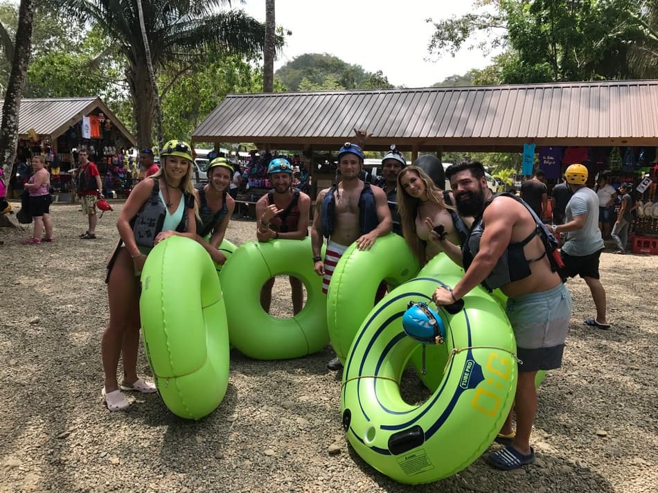 A group of seven people poses with green inflatable tubes at an outdoor adventure site.