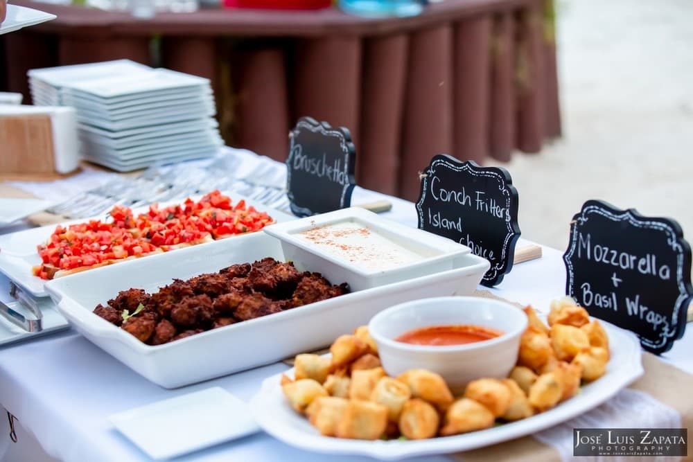 A table displays an assortment of appetizers, including bruschetta, conch fritters, and mozzarella basil wraps.