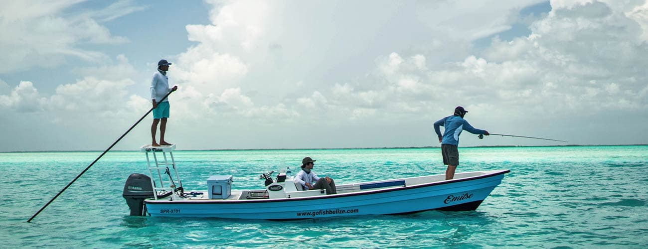 Two fishermen on a boat are fishing in clear turquoise waters under a cloudy sky.