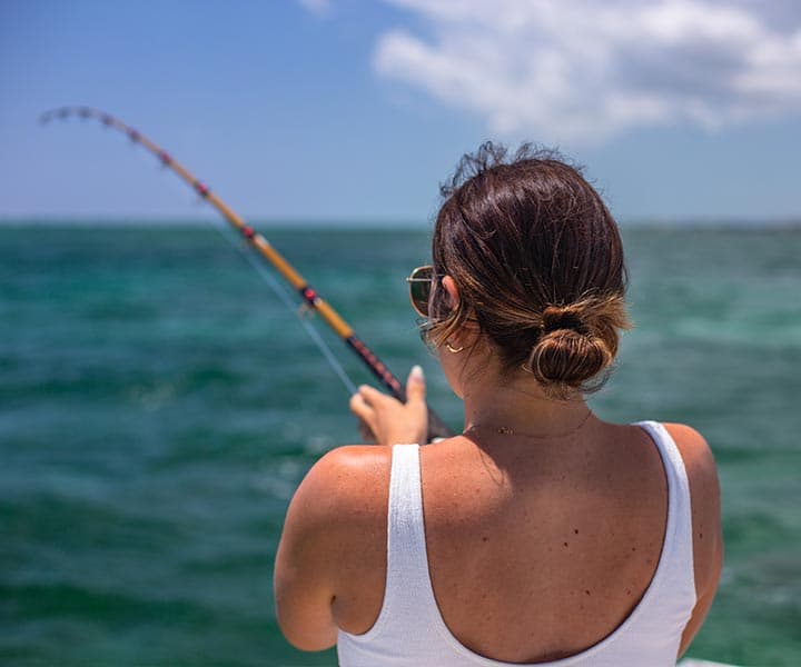 A woman in a tank top fishing off a boat in clear blue waters.