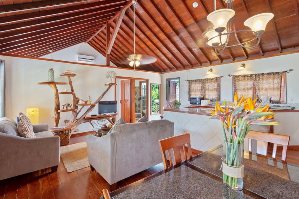 A cozy living space featuring a wooden ceiling, comfortable seating, and a dining area with a floral centerpiece.